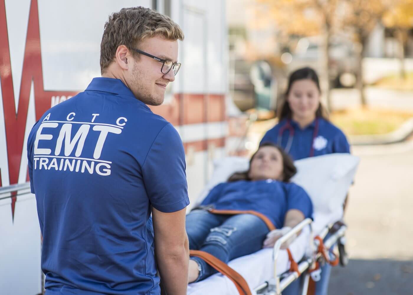 Three students learning how to use a stretcher during EMT training.