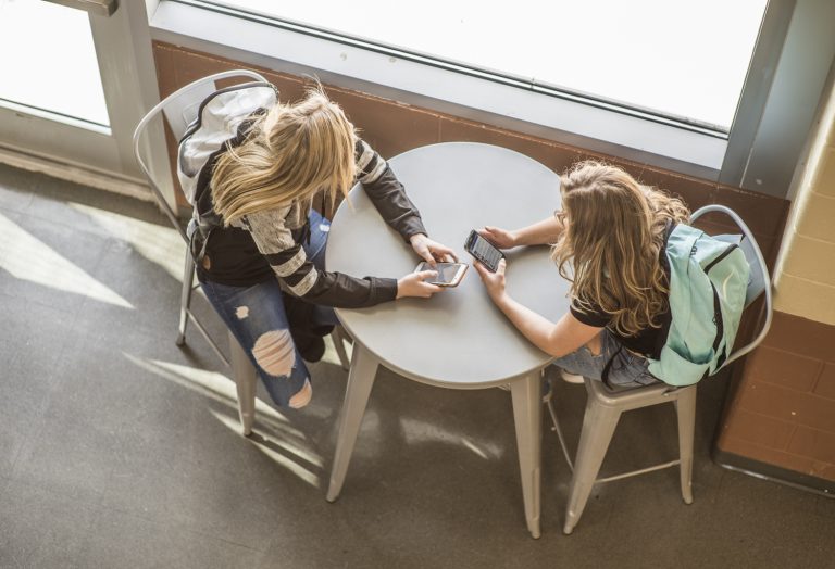 Two students sitting at a table looking at their smartphones.