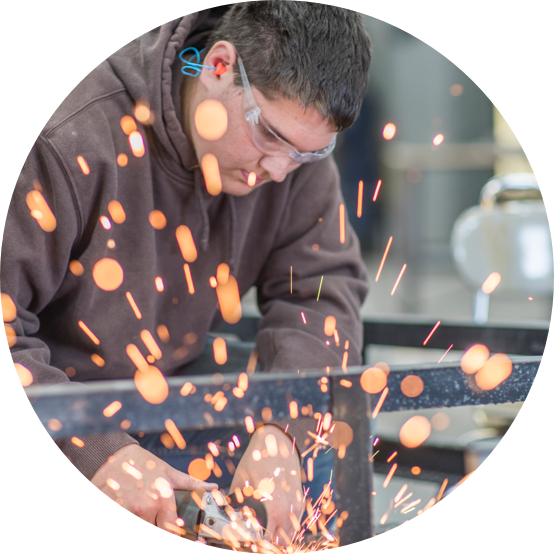 Closeup of man wearing goggles using a saw that is throwing colorful sparks.