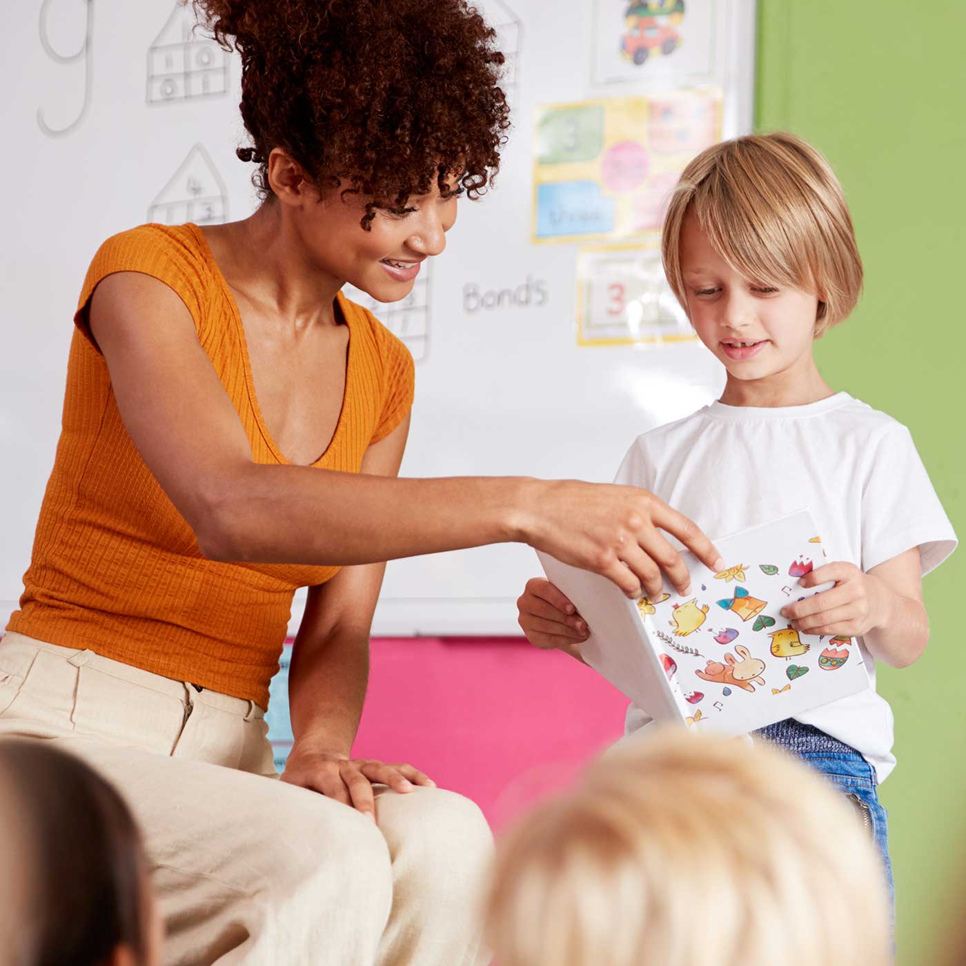 A teacher and young girl read a book to a group of students.