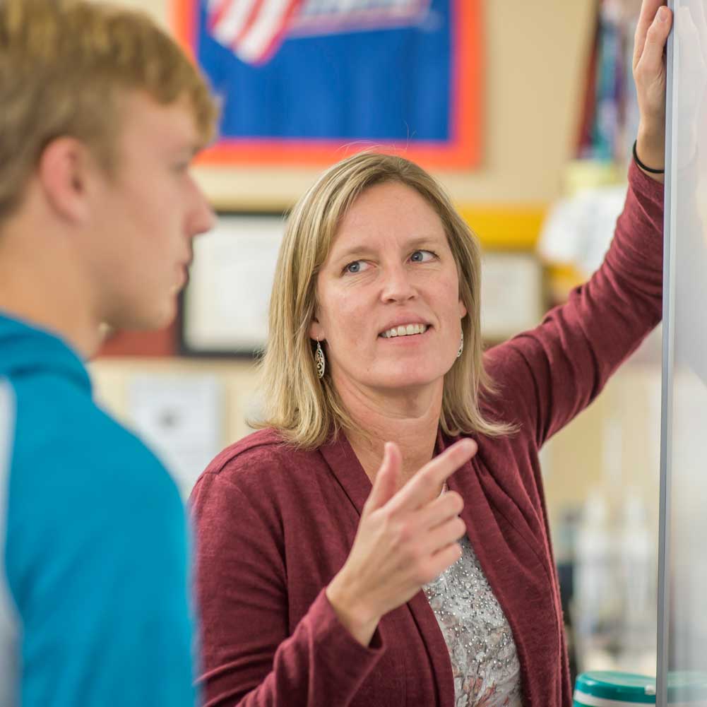 A teacher talking to a student in front of a whiteboard.